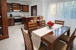 Een keuken met houten kastjes, een eettafel met stoelen en een raam met gordijnen.
