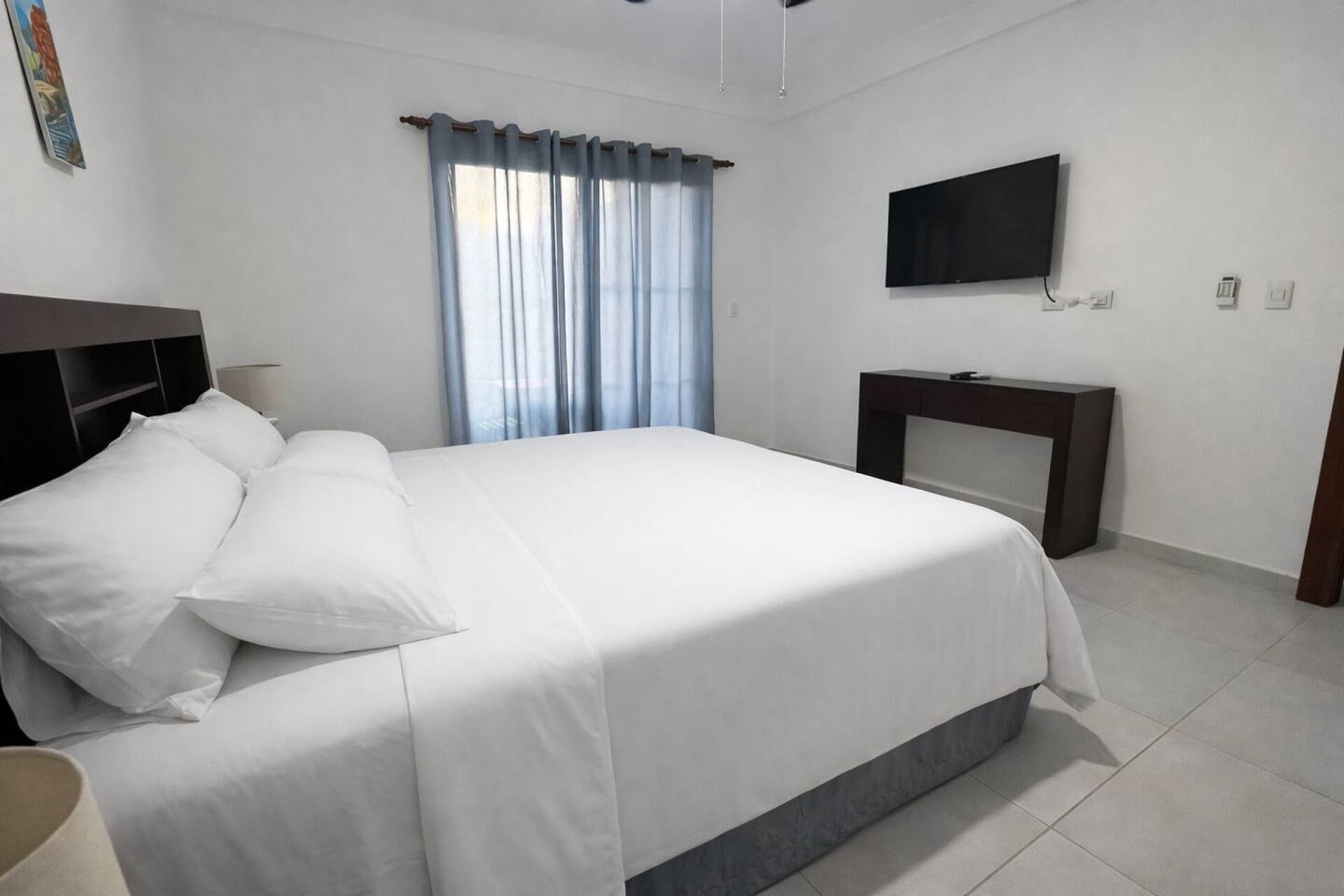 Habitación de hotel con cama, escritorio, televisor y ventana con cortinas.