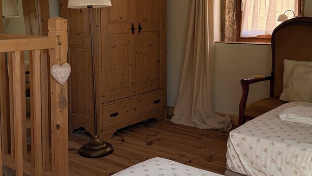 Une chambre avec deux lits, une armoire en bois, une lampe sur pied et une fenêtre avec des rideaux.