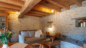 Une pièce chaleureuse avec un mur en pierre, des poutres apparentes, un canapé, une table et un vase rempli de fleurs.