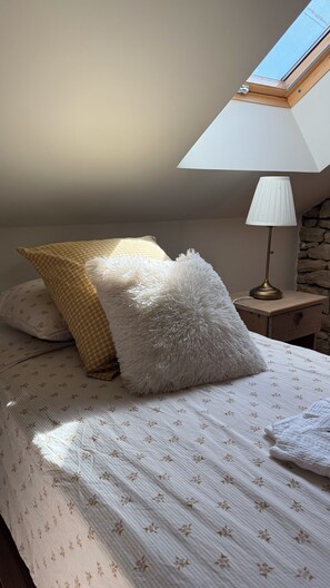 Un dormitorio con cama, dos almohadas, una mesita de noche con lámpara y un tragaluz.