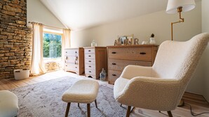 Une pièce chaleureuse avec un mur en pierre, une commode en bois, un fauteuil moelleux et une lampe.