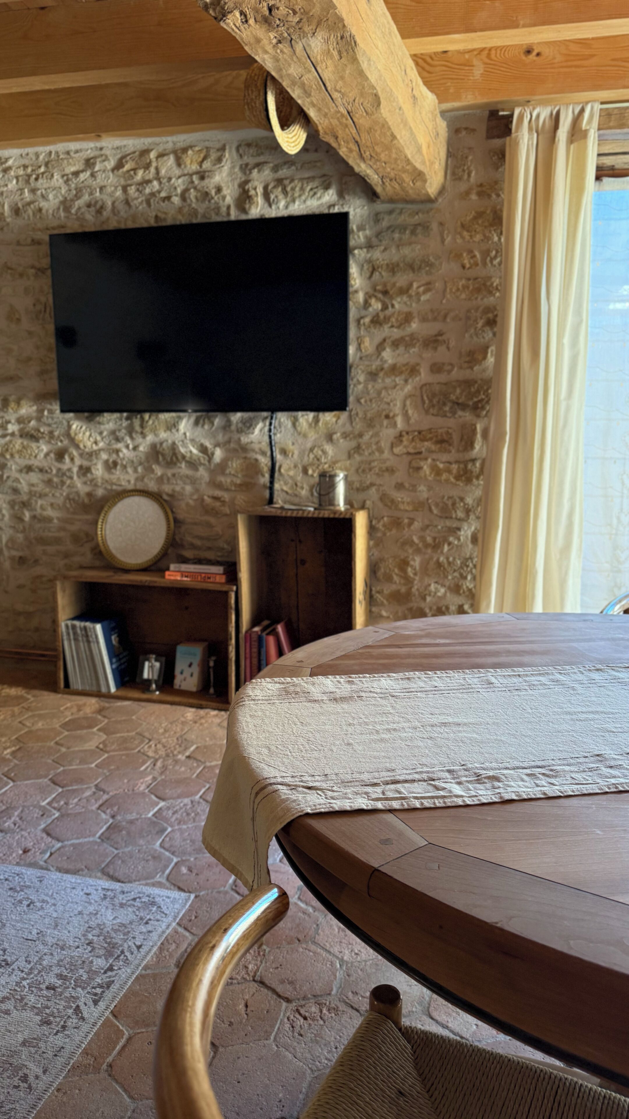 Ein Zimmer mit Steinwand, einem wandmontierten Flachbildfernseher, einem Holztisch mit gewebtem Tischläufer und einem Korbstuhl.