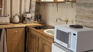 Une cuisine avec un mur en pierre, des meubles en bois, un réfrigérateur blanc et une machine à café.