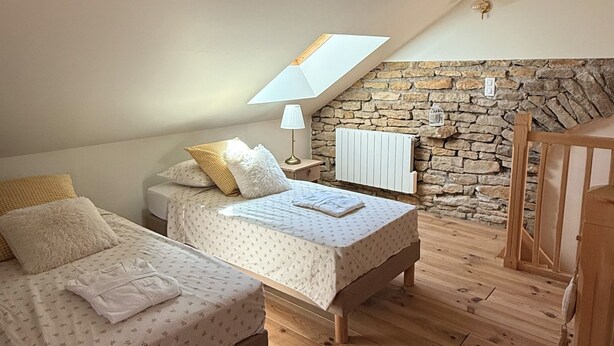 A bedroom with two beds, a stone wall, a sloped ceiling, and a wooden floor.