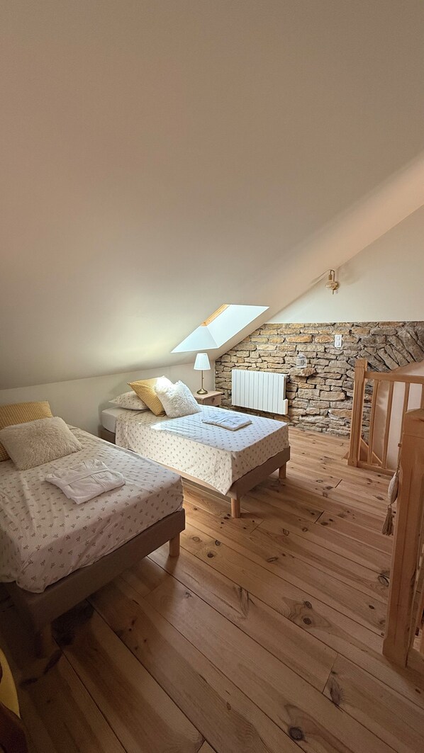 Un dormitorio con dos camas, una pared de piedra, techo inclinado y suelo de madera.