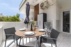 A round table with chairs, a vase with flowers, and a bottle on a balcony with a view of buildings and trees. - Club Atlantis 150 - One Bed (Costa Adeje)