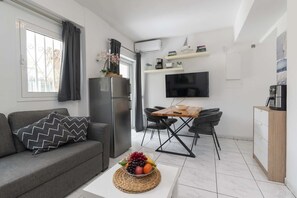 Ein kompakter Wohnbereich mit einer Couch, einem Esstisch mit Stühlen, einem Fernseher und einem Kühlschrank.