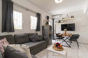 Ein modernes Wohnzimmer mit Sofa, einem Esstisch mit Stühlen, einem Kühlschrank und einem flachbildfernseher an der Wand.