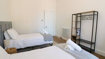 Une chambre d’hôtel avec deux lits, une armoire, un radiateur et une petite table.