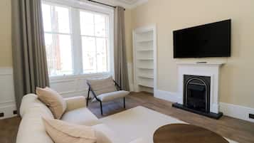 A living room with a sofa, a coffee table, a fireplace, a television, and a window with curtains.