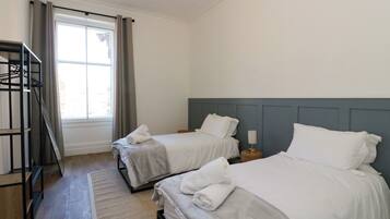 A hotel room with two beds, a window with curtains, a wooden floor, and a metal rack.