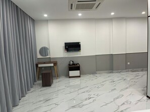 Een moderne hotelkamer met een flatscreen televisie aan de muur, een klein houten bijzettafeltje, een koffiezetapparaat en een vloer met een marmerlook.