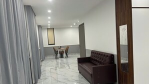 Ein modernes Hotelzimmer mit Marmorboden, einem braunen Ledersofa, einem Esstisch mit Stühlen und einem großen Spiegel.
