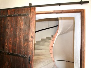 A wooden door with metal hinges and a white staircase with a striped handrail.