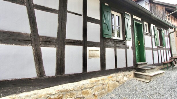 A traditional half-timbered building with a stone foundation, a green door, and a small set of steps leading to the entrance. - Schlossgut Franken (Redwitz an der Rodach)