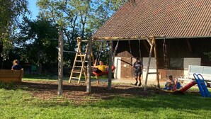 A playground with swings and a slide, a wooden bench, and a building with a sloped roof.