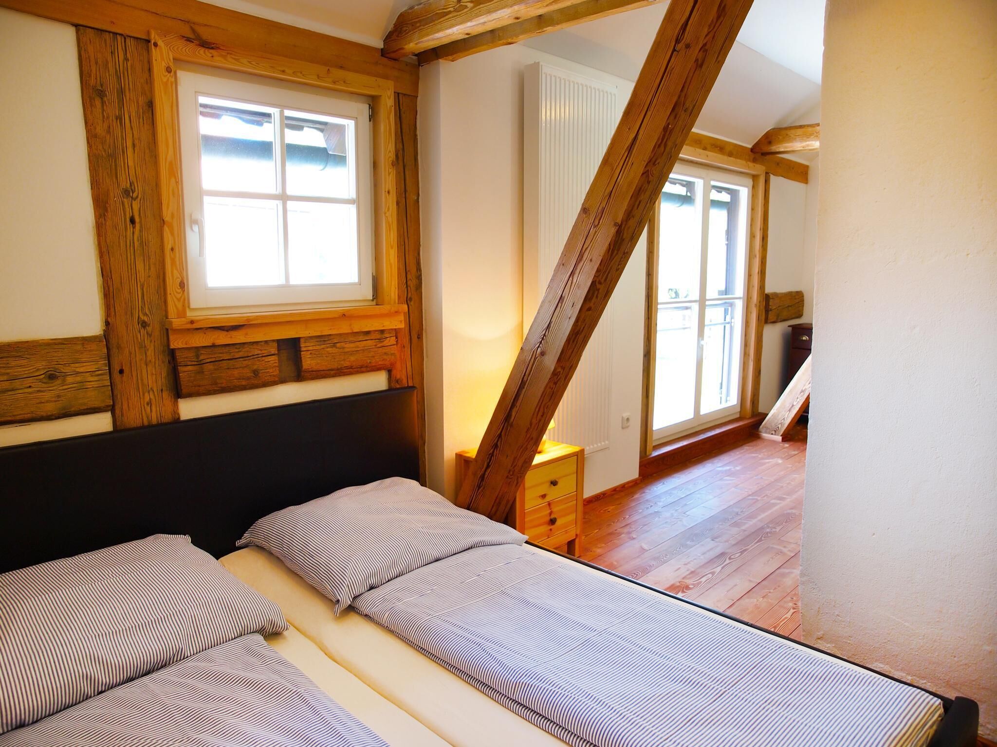 A bedroom with a bed, wooden beams, a window, and a radiator.