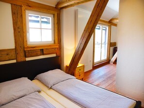 A bedroom with a bed, wooden beams, a window, and a radiator.