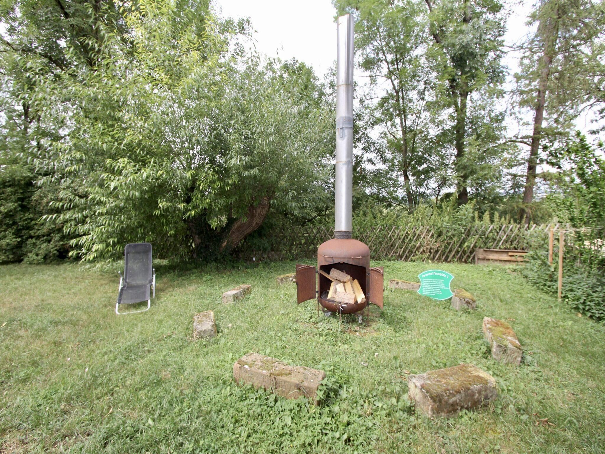 Un entorno rústico al aire libre con un hogar a leña, un poste de metal y un banco.