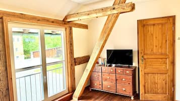 A room with a wooden ceiling, a sliding glass door, a TV on a wooden cabinet, and a wooden wardrobe.