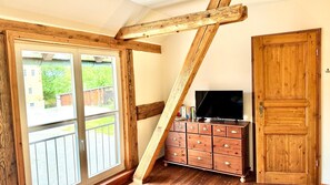 A room with a wooden ceiling, a sliding glass door, a TV on a wooden cabinet, and a wooden wardrobe.