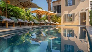 A pool area with lounge chairs and umbrellas, a building with shutters, and a reflection in the water. - Superbe appartement place des lices (Saint-Tropez)