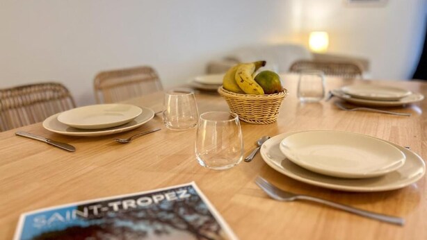 A dining table set with plates, cutlery, and a basket of fruit. - Superbe appartement place des lices (Saint-Tropez)