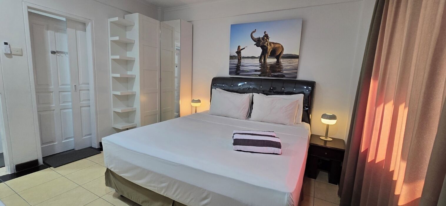 A hotel room with a bed, a wardrobe, a bedside table with a lamp, and a painting of an elephant.