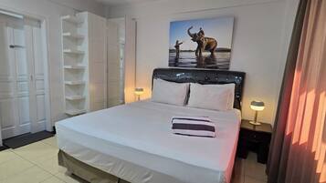 A hotel room with a bed, a wardrobe, a bedside table with a lamp, and a painting of an elephant.
