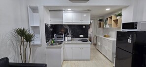 A compact kitchen with white cabinets, a black refrigerator, and a microwave.