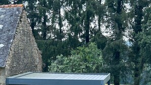 A stone building with a covered patio area, a table with a red and white tablecloth, and a small garden with a bush and a stone structure. - Holiday Home 'Bienvenue – Former Farmhouse 4 to 6 p' with Terrace, Garden & Wi-Fi (Ploërdut)