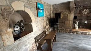 A stone-walled room with a fireplace, a bench, and a television. - Holiday Home 'Bienvenue – Former Farmhouse 4 to 6 p' with Terrace, Garden & Wi-Fi (Ploërdut)