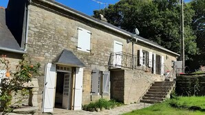 A stone building with a balcony, a staircase, and a door. - Holiday Home 'Bienvenue – Former Farmhouse 4 to 6 p' with Terrace, Garden & Wi-Fi (Ploërdut)