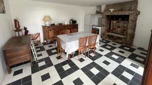 A dining area with a checkered floor, a table with chairs, a wooden cabinet, a microwave, and a stone fireplace. - Holiday Home 'Bienvenue – Former Farmhouse 4 to 6 p' with Terrace, Garden & Wi-Fi (Ploërdut)