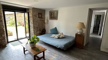 Une pièce spacieuse comprenant un lit, une table avec une plante et une vue sur l’extérieur, accessible par une porte vitrée.