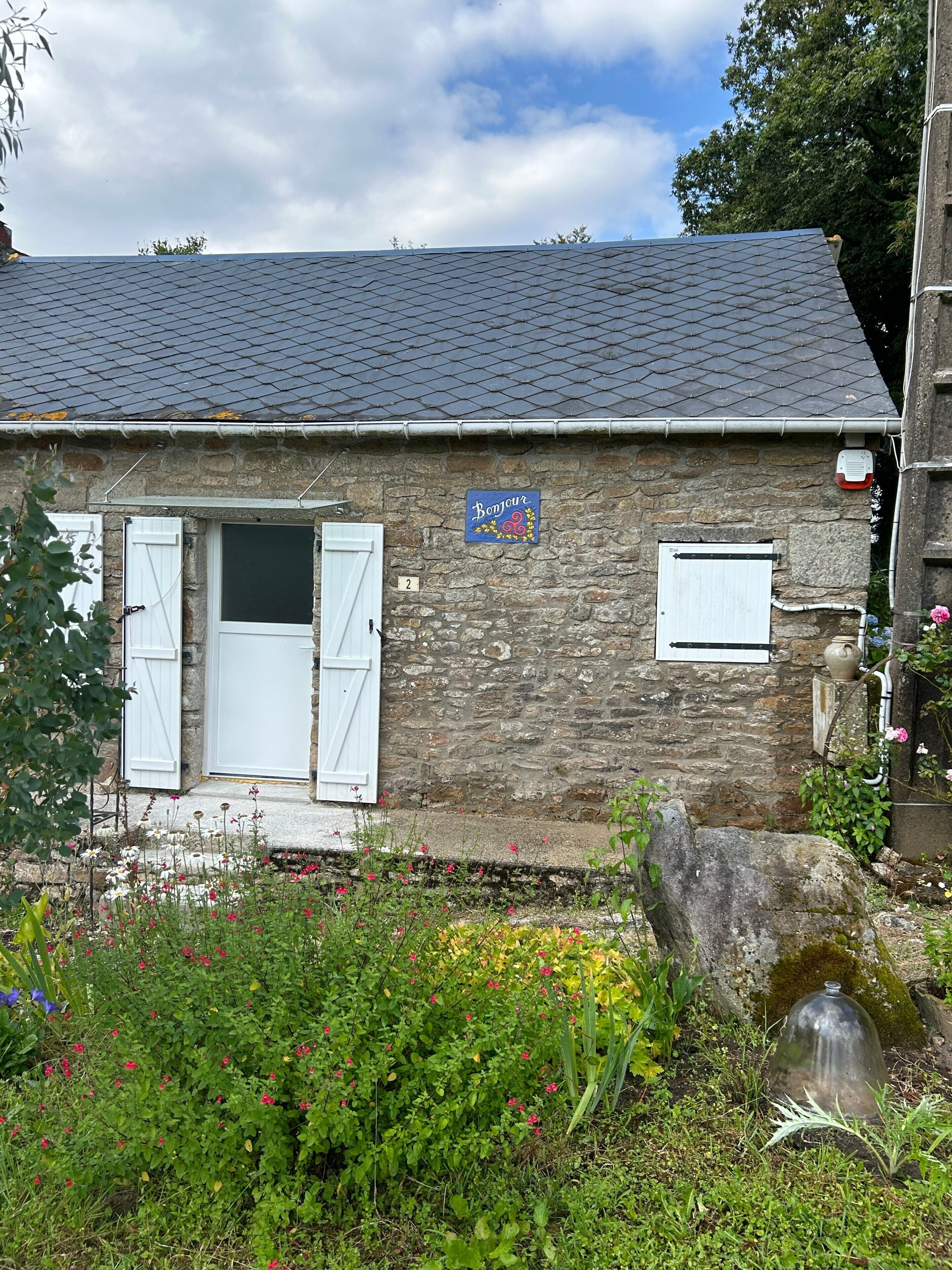 A stone building with a 'Bonjour' sign, a white door, and a small window.