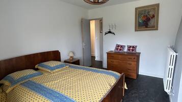 Un dormitori amb llit de fusta, un taulell, un radiador i una porta que dona a una altra habitació.