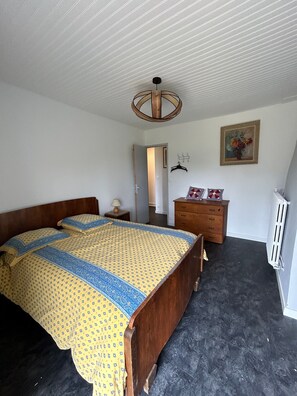 Ein Schlafzimmer mit einem hölzernen Bett, einem Schminktisch, einem Heizkörper und einer Tür zu einem anderen Raum.
