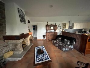 Una sala de estar con chimenea, un revestimiento de piedra alrededor de la chimenea, una mesa de centro de madera con un mantel decorado y un sofá con funda estampada.