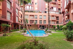 A multi-story residential building with a central courtyard featuring a swimming pool, surrounded by greenery and palm trees. - Superbe face Jardin Majorelle | Piscine & Parking (Marrakesh)