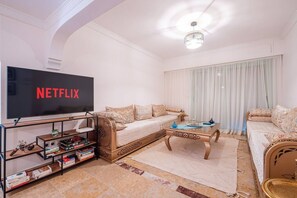 A living room with a flat-screen TV, a sofa, a coffee table, and a bookshelf. - Superbe face Jardin Majorelle | Piscine & Parking (Marrakesh)