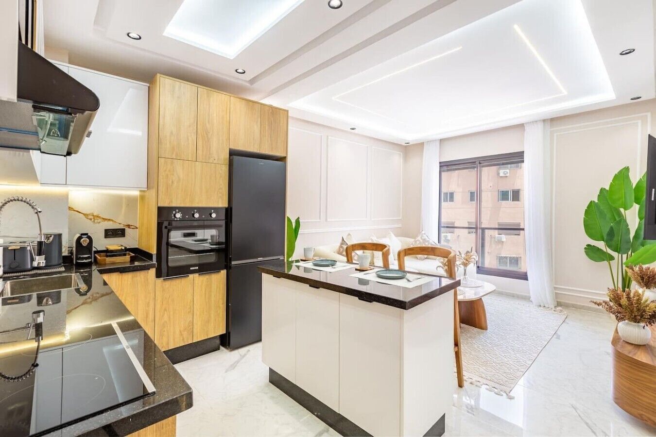 Une cuisine moderne dotée d’un îlot central, d’un four encastré et d’une grande fenêtre offrant une vue sur la ville.