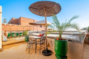 Terrassa exterior amb taula i cadires, un parasol gran i plantes en testos.