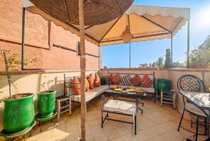 Een terras buiten met een tafel, stoelen, een bank en potplanten.