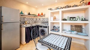 Eine kompakte Küche mit Waschmaschine, Kühlschrank und Esstisch mit kariertem Tischläufer.
