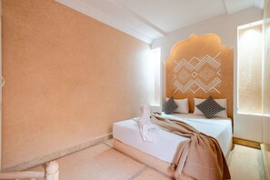Een slaapkamer met een bed, kussens, een hoofdbord met een geometrisch patroon en een raam met gordijnen.