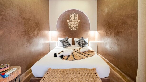 Ein Hotelzimmer mit einem Bett, einem an der Wand befestigten Behindertensymbol und einem kleinen Tisch mit einer Fernbedienung.