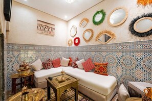 A room with a patterned tile wall, a sofa with cushions, a small table with a lamp, and decorative mirrors on the wall. - Riad Jad • 5BR • Pool • Breakfast • Rooftop (Marrakesh)