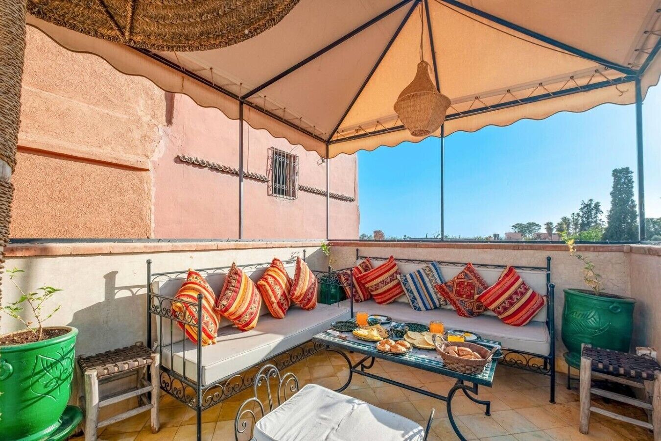 Une terrasse sur le toit avec un espace salon couvert, une table garnie de nourriture et des plantes en pot.